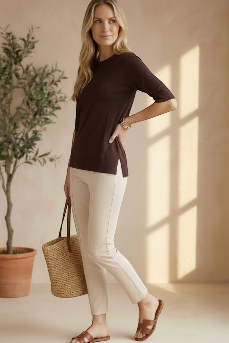Model wearing a graced espresso brown short sleeve knit top with side slits, paired with beige trousers and sandals.
