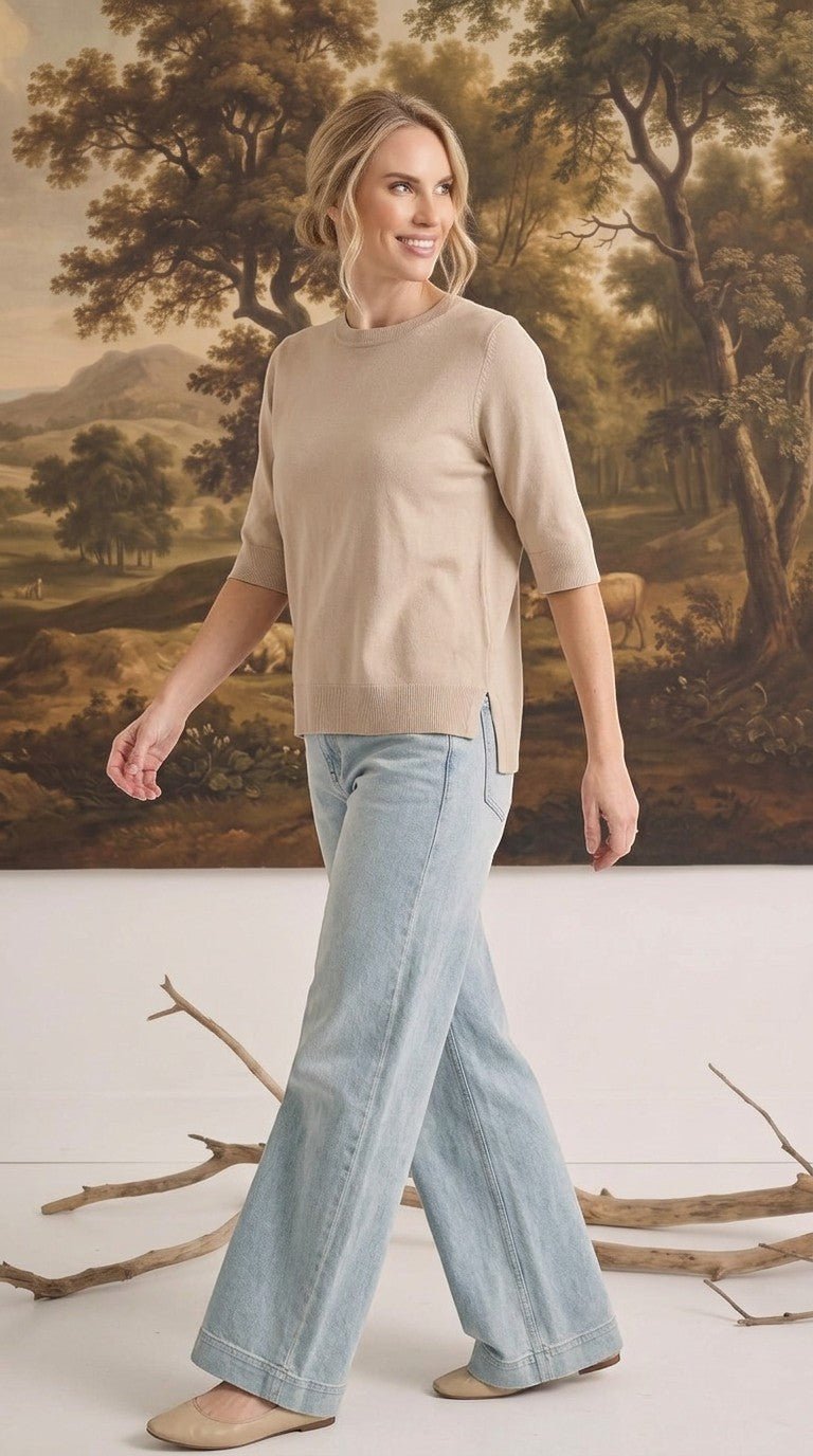 Model wearing a graced oatmeal short sleeve knit top with a crew neck and side slits, paired with light wash jeans.