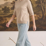 Model wearing a graced oatmeal short sleeve knit top with a crew neck and side slits, paired with light wash jeans.
