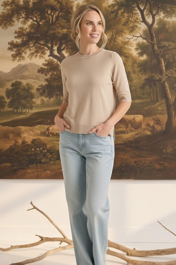 Model wearing a graced oatmeal short sleeve knit top with a crew neck and light wash jeans in a studio setting.