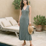 Woman in a green dress standing by a poolside with a lounge chair and plants.