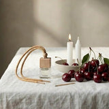 Table setting with candles, cherries, and a diffuser on a white tablecloth.