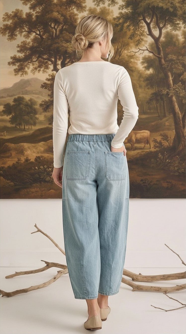 Back view of a woman wearing graced light wash soft denim barrel pants with an elastic waist and patch pockets.