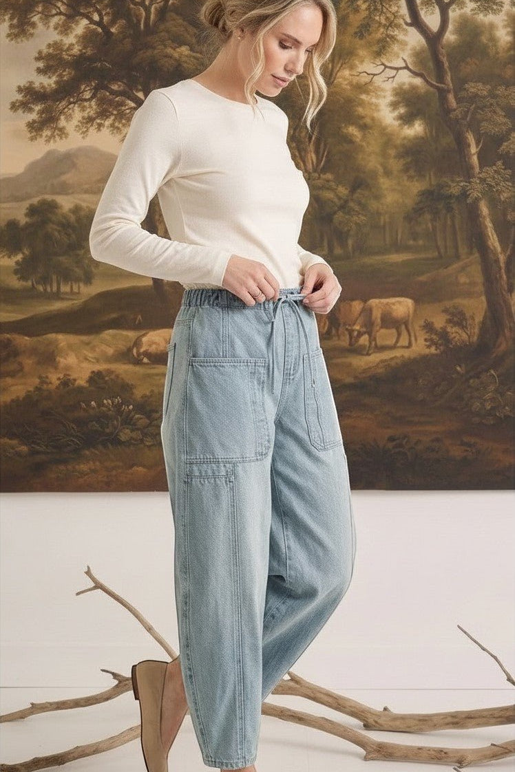 Model wearing graced light wash denim barrel pants with a relaxed fit, high waist, and large patch pockets