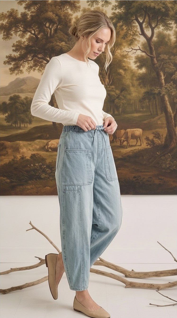 Model wearing graced light wash denim barrel pants with a relaxed fit, high waist, and large patch pockets