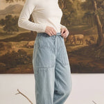 Model wearing graced light wash denim barrel pants with a relaxed fit, high waist, and large patch pockets