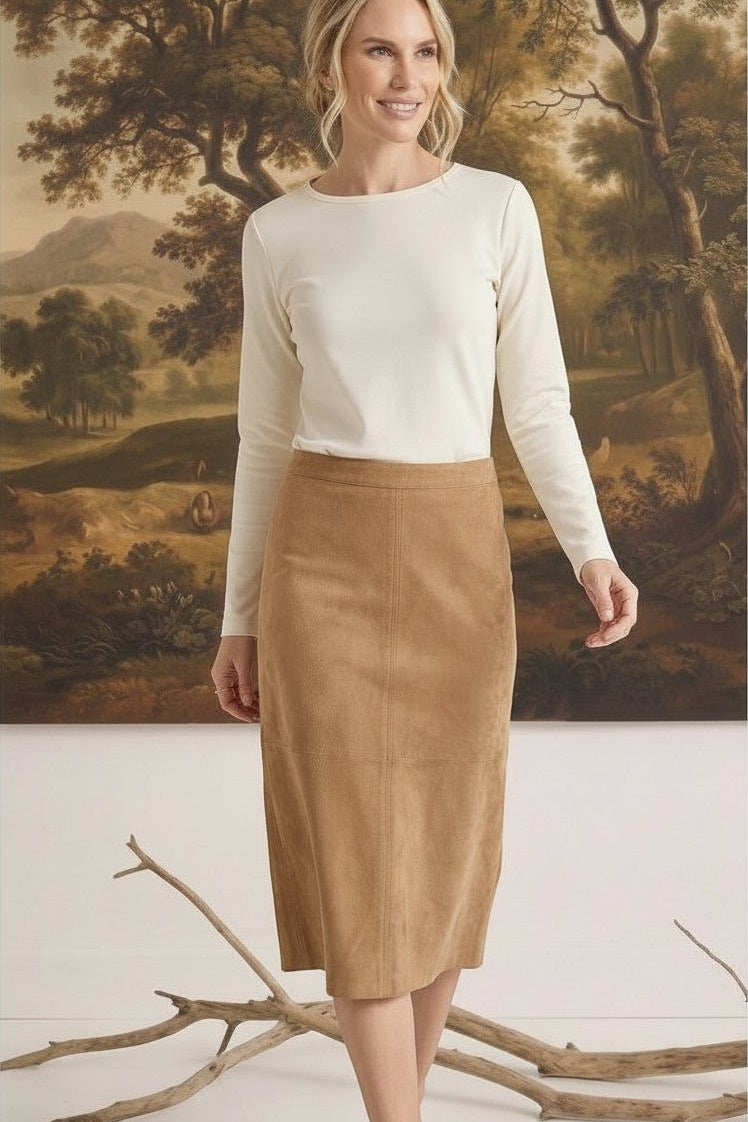 A model wearing a graced tan suede A-line skirt paired with a long-sleeve cream top in a studio setting.