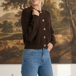 Woman wearing a dark brown textured button down cardigan by graced paired with blue jeans in a studio setting