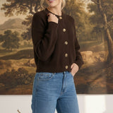 Woman wearing a dark brown textured button down cardigan by graced paired with blue jeans in a studio setting