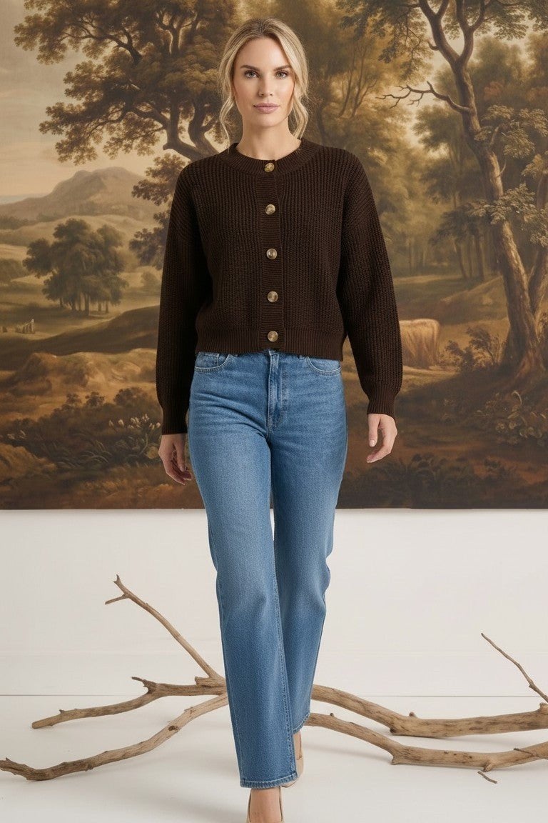 Model wearing a graced dark brown textured button down cardigan with blue jeans and beige heels in a studio setting.