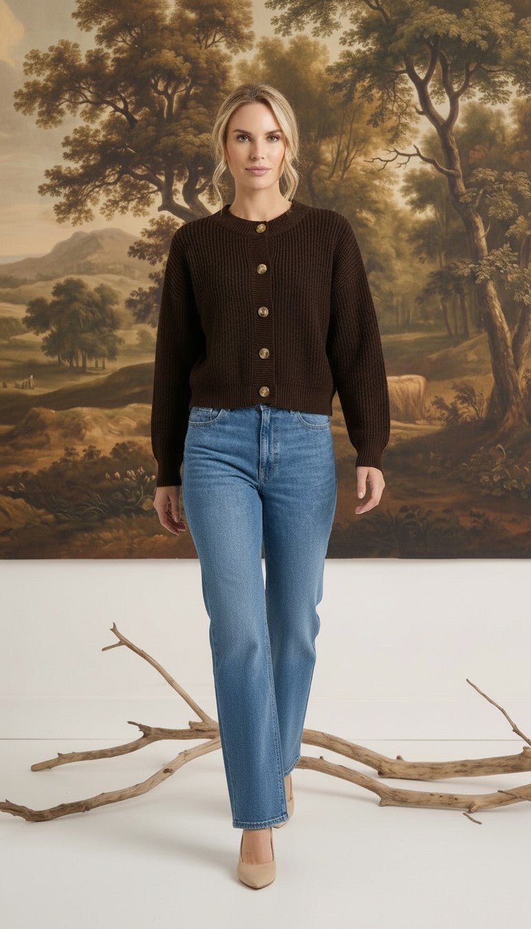 Model wearing a graced dark brown textured button down cardigan with blue jeans and beige heels in a studio setting.