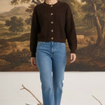Model wearing a graced dark brown textured button down cardigan with blue jeans and beige heels in a studio setting.