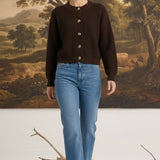Model wearing a graced dark brown textured button down cardigan with blue jeans and beige heels in a studio setting.