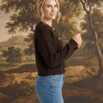 A woman wearing a graced dark brown textured button-down cardigan with blue jeans in a side profile view.