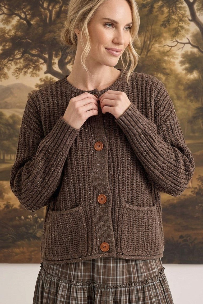 Model wearing a graced brown ribbed knit cardigan with raw edges, button front, and pockets over a plaid skirt
