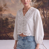 graced white April Embroidery Blouse with intricate needlework, V-neck, and puff sleeves worn with light wash jeans