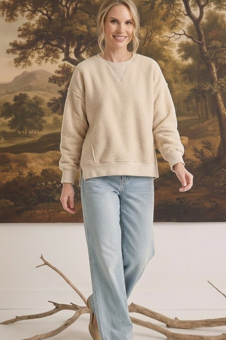 Model wearing a cream oversized brushed fleece top from graced, paired with light wash jeans in a studio setting.