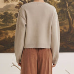 A woman wearing a beige graced Baylie cardigan from the back, featuring a ribbed hem and relaxed fit.