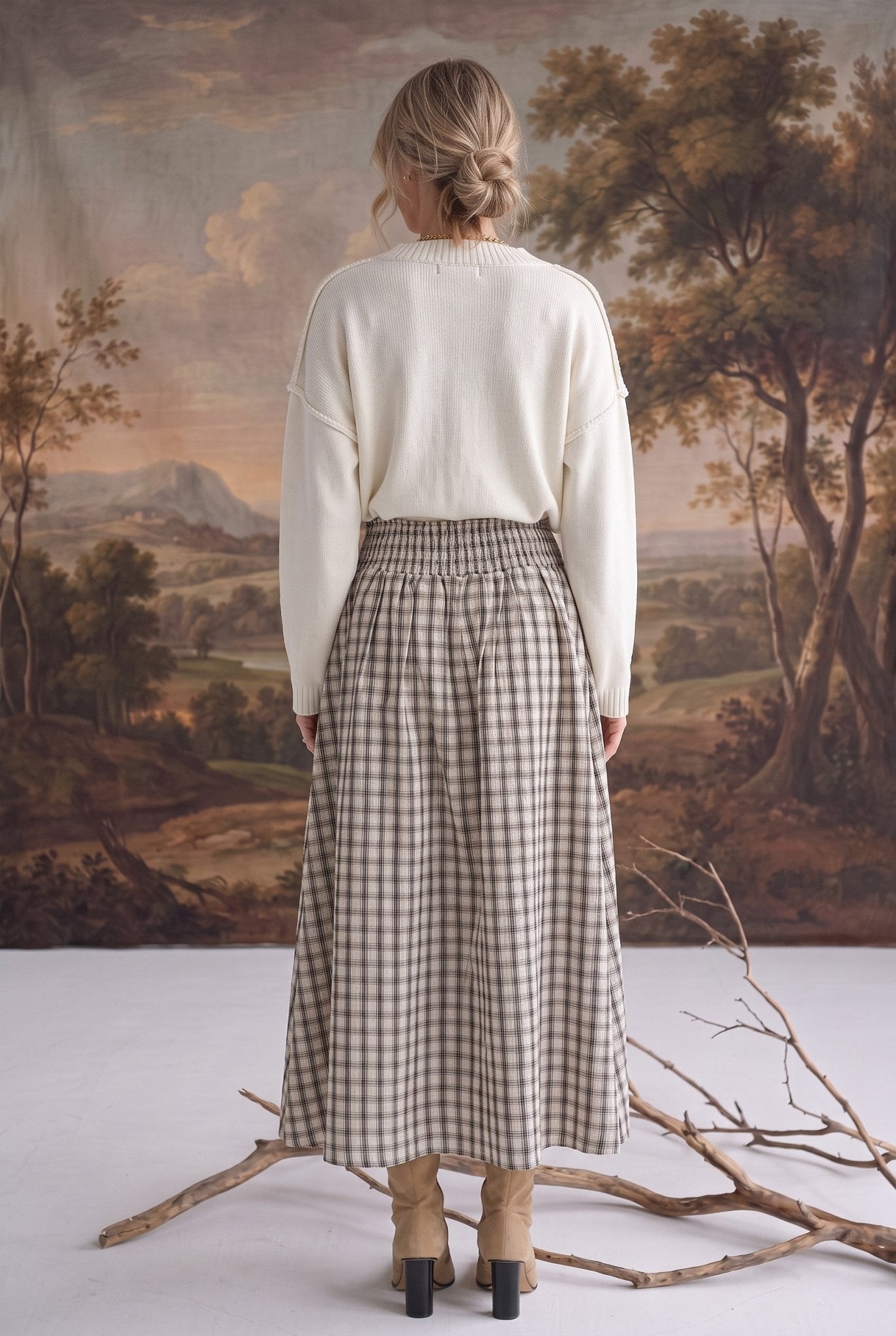 Back view of a model wearing the graced Beatrice plaid cotton midi skirt with a smocked waist and cream sweater.