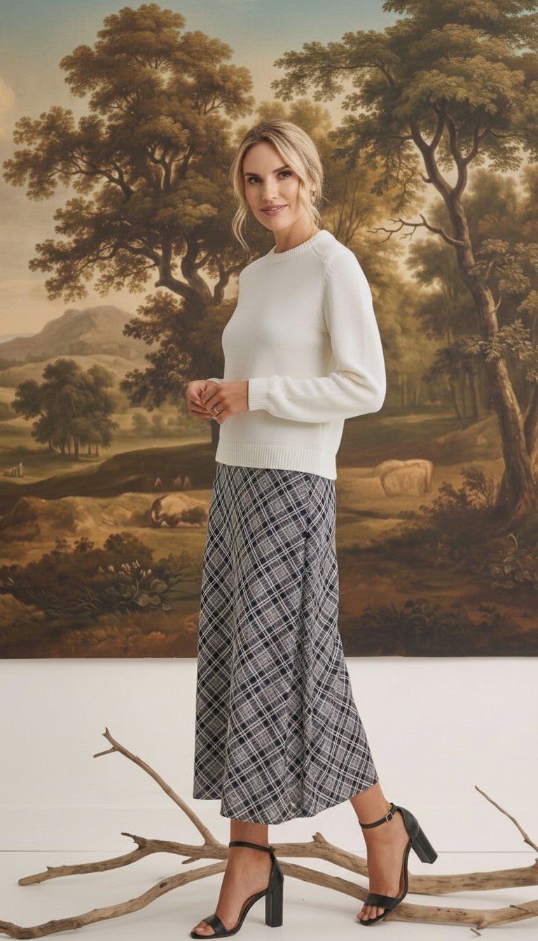 A model wearing a graced Beth plaid midi skirt with a white sweater and black heels in a studio setting.