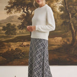 A model wearing a graced Beth plaid midi skirt with a white sweater and black heels in a studio setting.