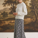 A model wearing a graced Beth plaid midi skirt with a white sweater and black heels in a studio setting.