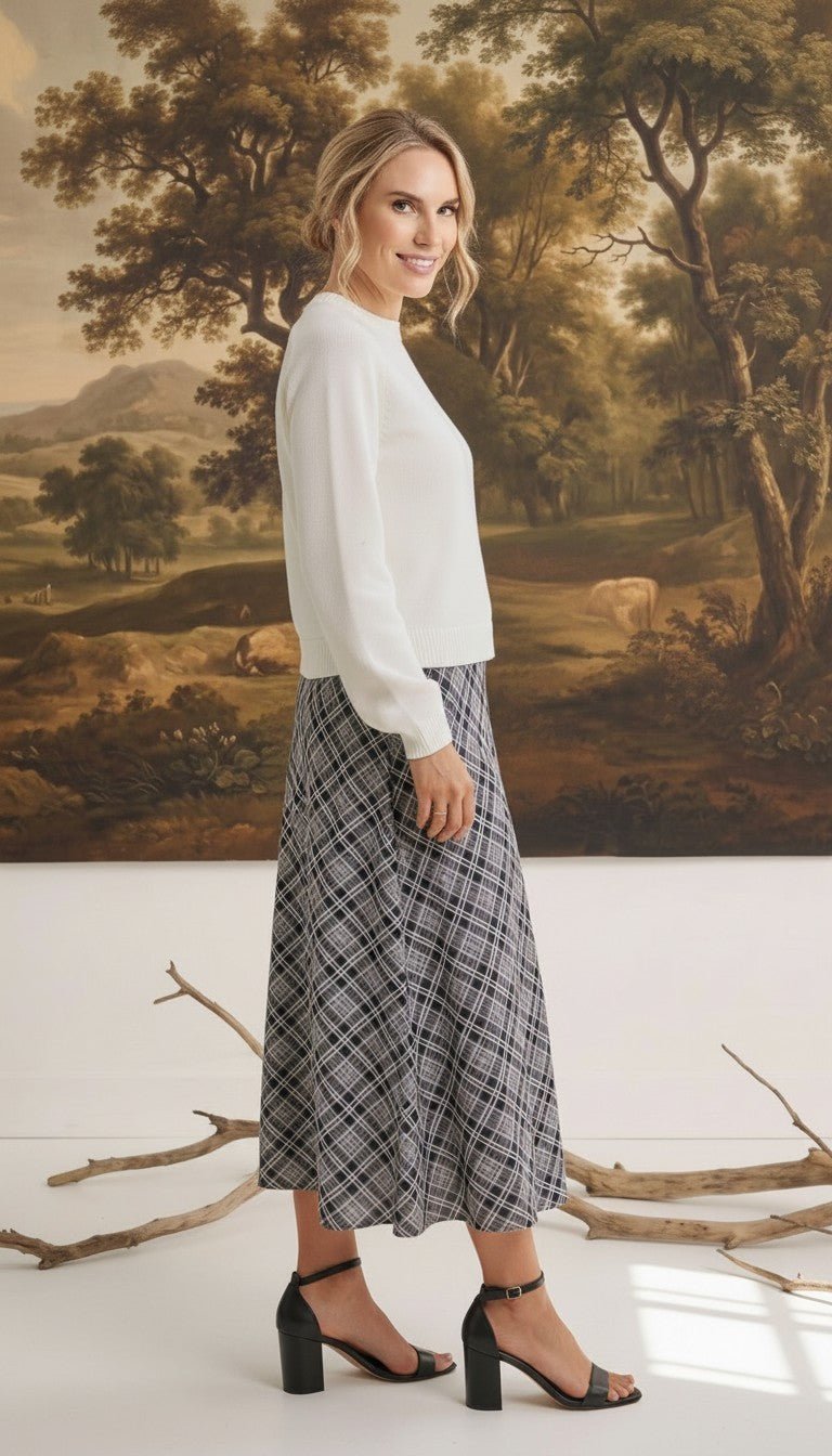 Model wearing a graced Beth plaid midi skirt with an A-line silhouette, paired with a white sweater and black heels.