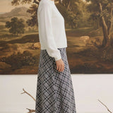 Model wearing a graced Beth plaid midi skirt with an A-line silhouette, paired with a white sweater and black heels.