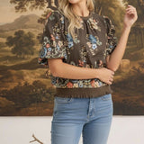 Model wearing graced brown floral top with puff sleeves and ribbed waist, styled with blue jeans.