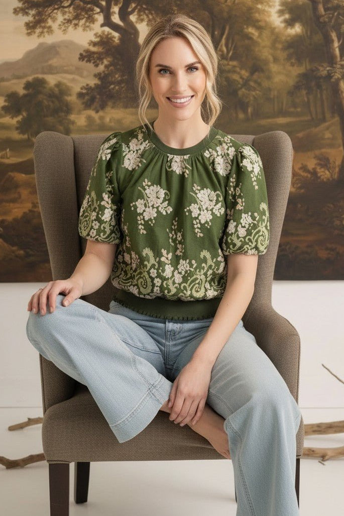 graced Brenda floral top in olive green with puff sleeves and embroidered details worn by a woman in a chair