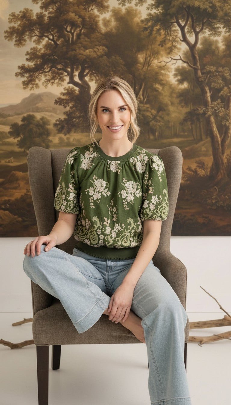 graced Brenda floral top in olive green with puff sleeves and embroidered details worn by a woman in a chair