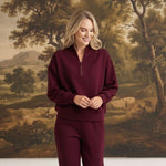 graced model wearing a dark cherry ribbed quarter-zip sweater with matching pants against a scenic landscape mural