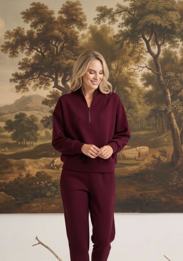 graced model wearing a dark cherry ribbed quarter-zip sweater with matching pants against a scenic landscape mural