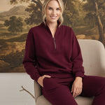 graced Brooklyn Rib quarter zip sweater in dark cherry worn by a smiling woman sitting on a chair