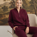 graced Brooklyn Rib quarter zip sweater in dark cherry worn by a smiling woman sitting on a chair