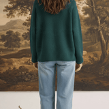 Back view of a model wearing the graced Carley Mallard Sweater in forest green with light wash jeans