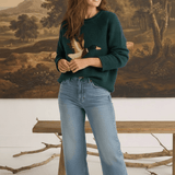 Model wearing a graced Carley Mallard forest green knit sweater with a duck motif, paired with light wash jeans.