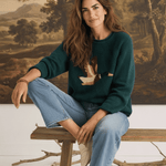 graced Carley Mallard sweater in forest green with a duck motif, worn by a woman with light blue jeans and loafers.
