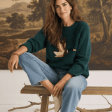 graced Carley Mallard sweater in forest green with a duck motif, worn by a woman with light blue jeans and loafers.