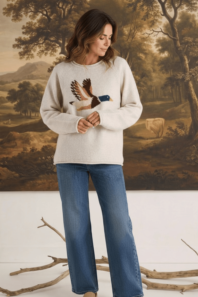 Model wearing a graced oatmeal knit sweater featuring a mallard duck design, paired with blue jeans and loafers.