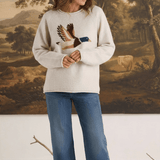 Model wearing a graced oatmeal knit sweater featuring a mallard duck design, paired with blue jeans and loafers.