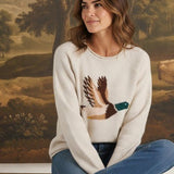 Model wearing graced Carley Mallard oatmeal knit sweater with duck graphic, blue jeans, and beige loafers.