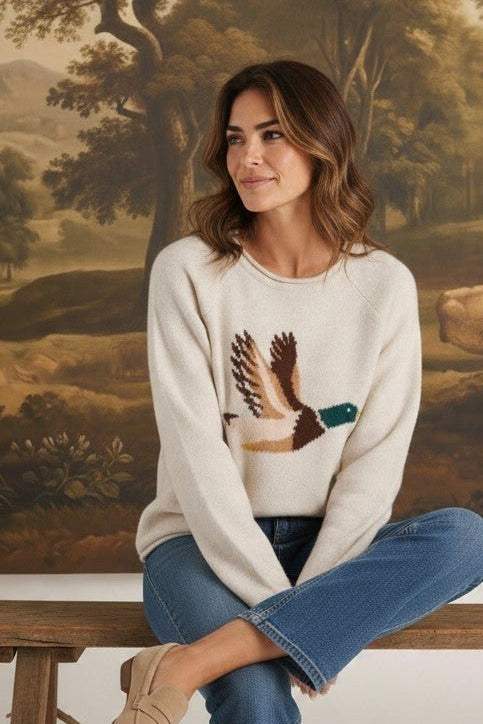 Model wearing graced Carley Mallard oatmeal knit sweater with duck graphic, blue jeans, and beige loafers.