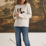 A model wearing a graced oatmeal-coloured knit sweater with a mallard duck design, paired with blue jeans and loafers.