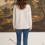 Back view of a woman wearing a graced Carley Mallard oatmeal sweater with blue jeans and white sneakers