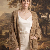 Model wearing a graced olive chunky knit cardigan with front pockets over a cream camisole and trousers