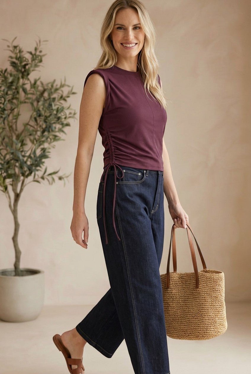 Model wearing a graced winetasting cotton top with side tie detail and sleeveless silhouette with dark denim jeans
