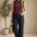A woman wearing a graced winetasting cotton top with side tie detail and dark denim jeans in a studio setting.