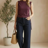 A woman wearing a graced winetasting cotton top with side tie detail and dark denim jeans in a studio setting.