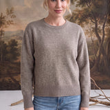 Woman wearing a graced taupe crew neck sweater with ribbed cuffs and hem, styled with blue jeans.